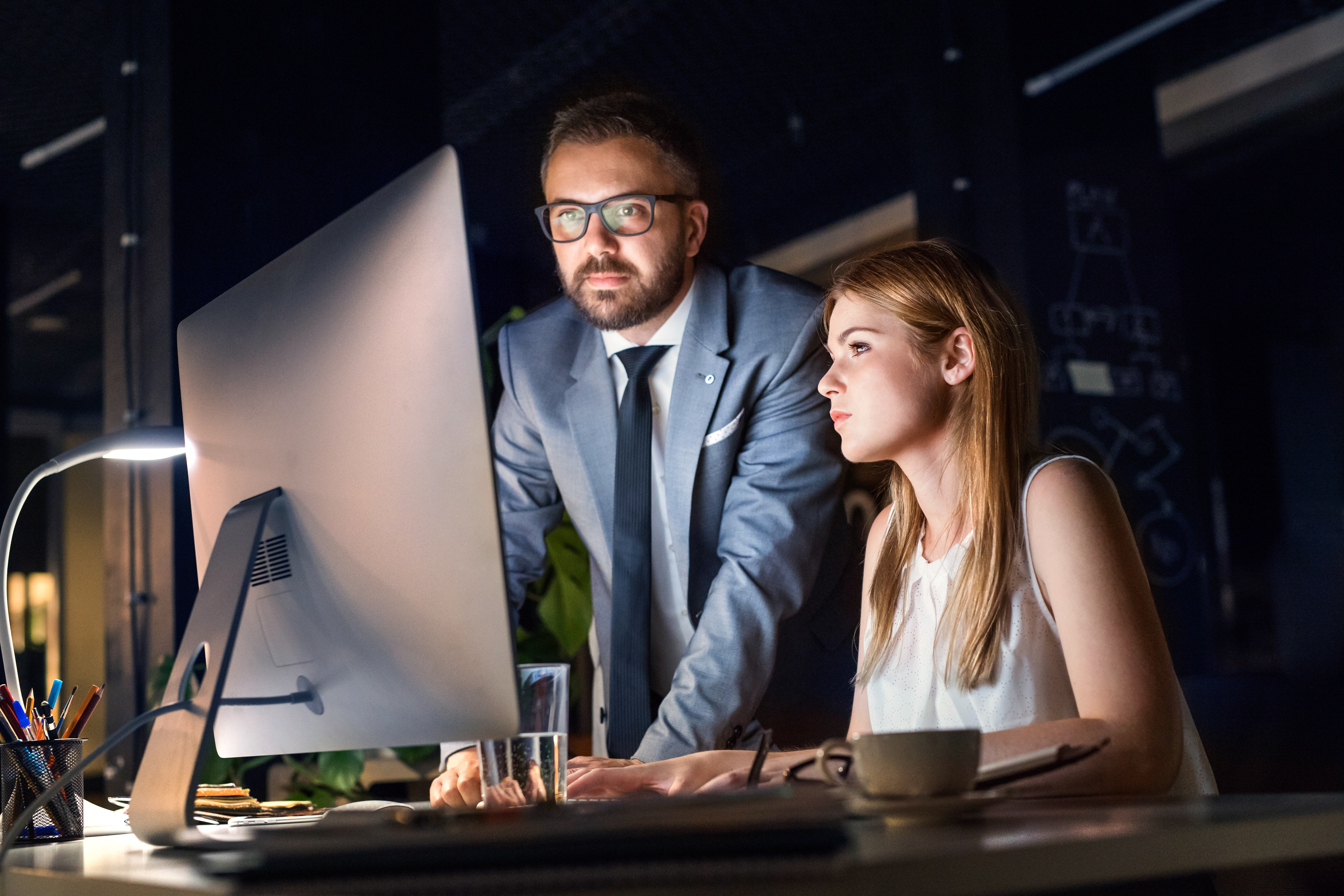 Two professionals at a dark-office workstation reviewing security strategy on screen